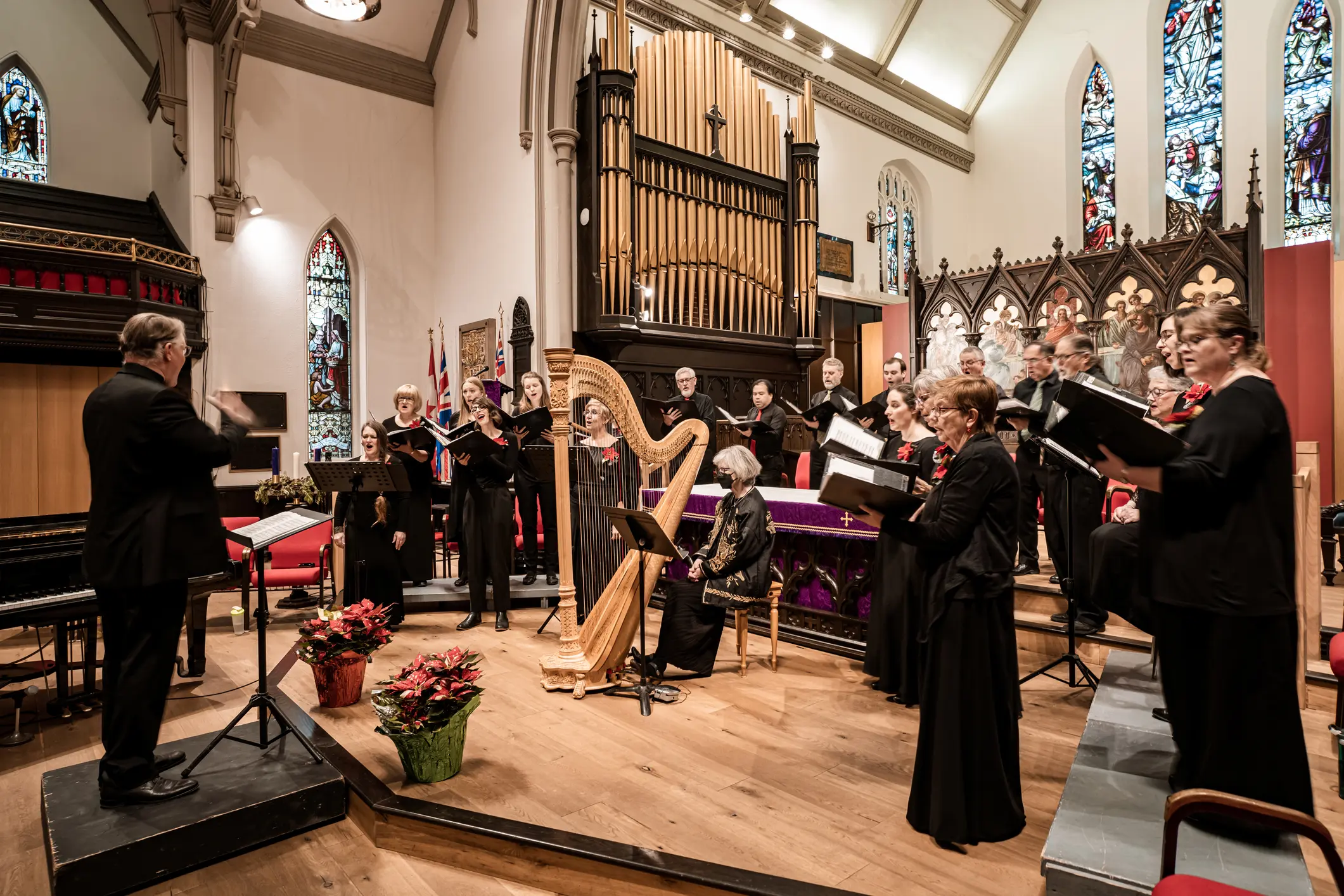 Orchestra and choir perform in a church with stained glass windows.